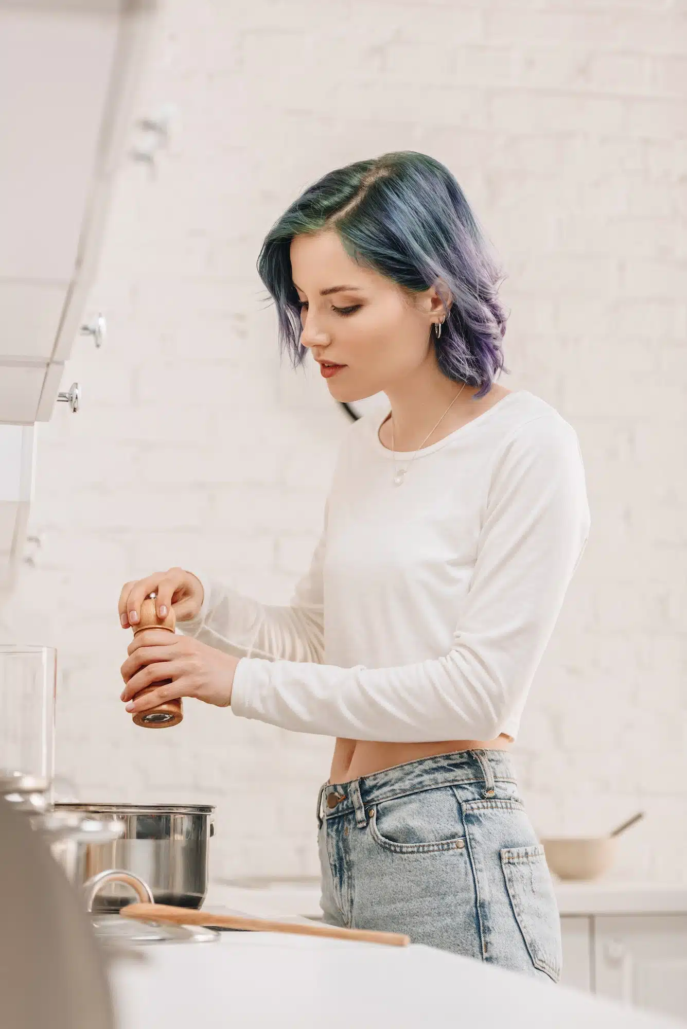 Selective focus of girl with colorful hair holding salt mill above pan on kitchen